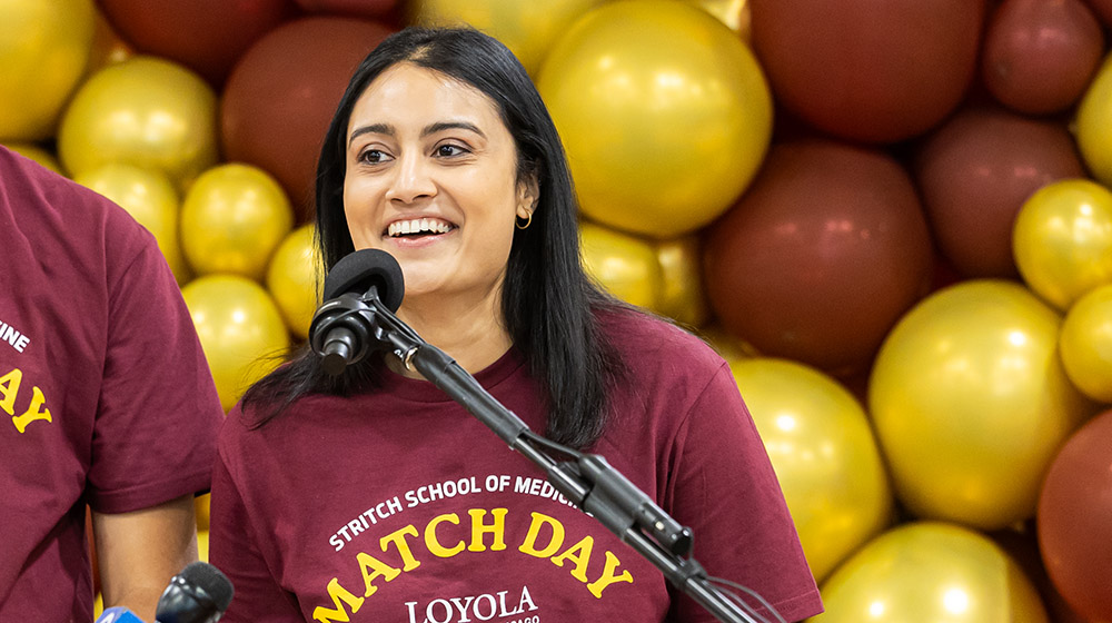 Samantha Swamy wearing a maroon Match Day t-shirt and speaking into a microphone